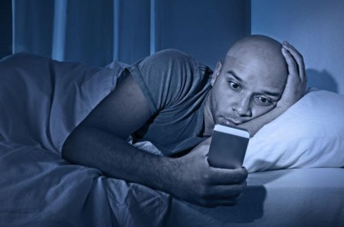 Mand kigger på sin mobil i sengen og kan risikere at få søvnmangel
