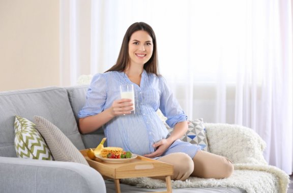 gravid kvinde der sidder i en sofa med mad