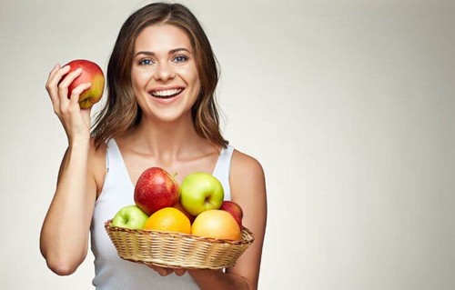 Glad kvinde holder en kurv med æbler 