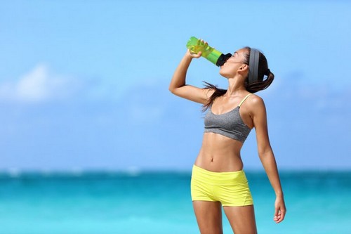 Kvinde drikker en flaske vand på stranden 