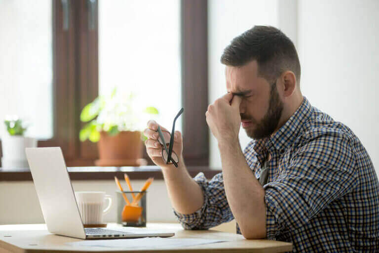 mand med hovedpine foran computer