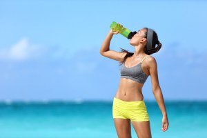 Une femme à la plage qui fait fait du sport et s'hydrate.