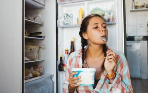 Une femme qui mange du yaourt devant son frigo ouvert. 