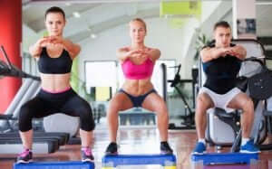 Trois personnes qui font des squats dans une salle de sport. 