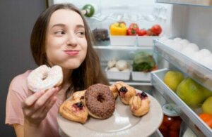Une jeune femme qui mange des donuts dans le frigo. 