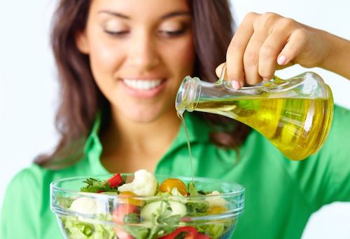 Ragazza che versa olio d'oliva nell'insalata 