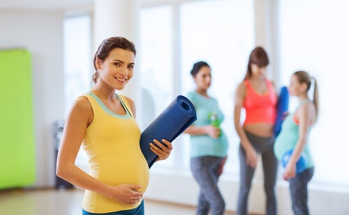 Signora con pancione sorride prima di un allenamento di pilates in gravidanza