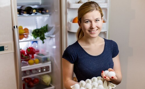 Ragazza sorride davanti al frigo tenendo delle uova
