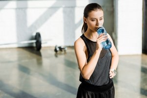 Kvinne drikker vann i treningssal.