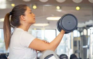 Kvinne trener bicepscurl med manual på treningsstudio.