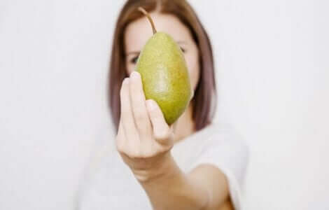 En kvinne som holder en pære for å vise en av de beste fruktene å spise om sommeren