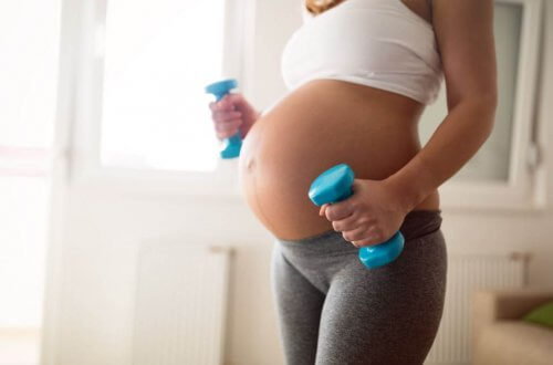 Zwangere vrouw met blote buik houdt dumbbells vast