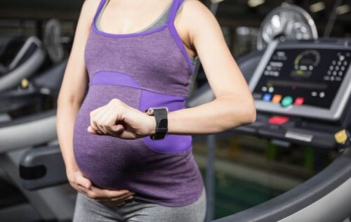 zwangere vrouw op loopband kijkt op horloge 