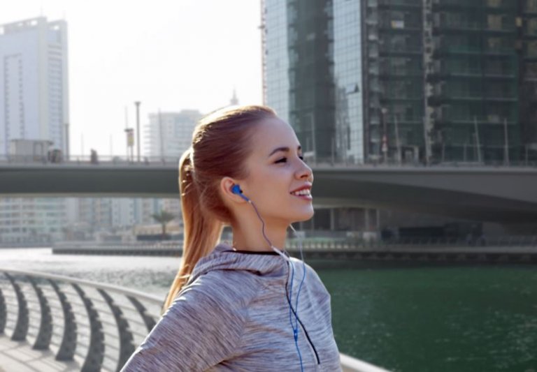 Uśmiechnięta kobieta w mieście ze słuchawkami w uszach