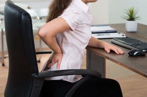 problemy z kręgosłupem - kobieta z bólem krzyża przy komputerze