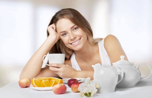 Uśmiechnięta kobieta przy stole z herbatą i owocami - jak przyspieszyć przemianę materii