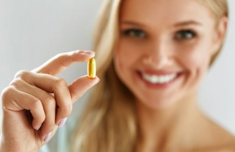 L-karnityna w tabletce i trzymająca ją, uśmiechnięta kobieta