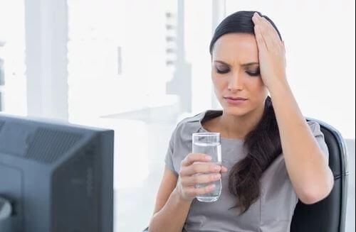 Dieta makrobiotyczna - odwodniona Kobieta trzymająca szklankę wody i przykładająca dłoń do głowy
