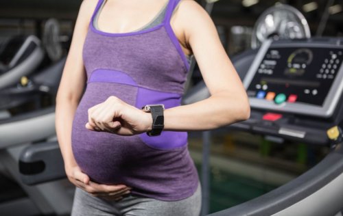 Kobieta w ciąży przy bieżni patrząca na zegarek - bieganie w ciąży