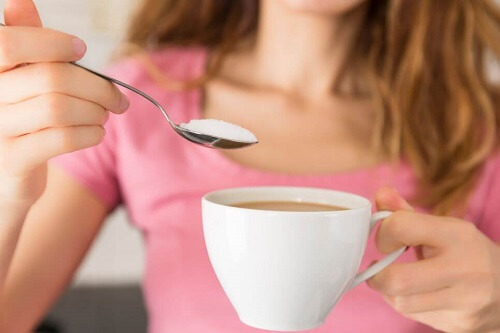 Kobieta wrzucająca do kawy łyżeczkę cukru - kofeina
