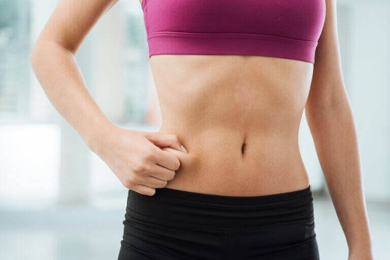 Kobieta łapiąca skórę na brzuchu - jak spalać tłuszcz i budować mięśnie