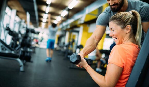 Kobieta z instruktorem na siłowni - czy ćwiczenia mogą szkodzić zdrowiu?