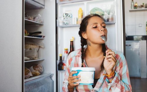Menina comendo iogurte com a geladeira aberta direto do pote