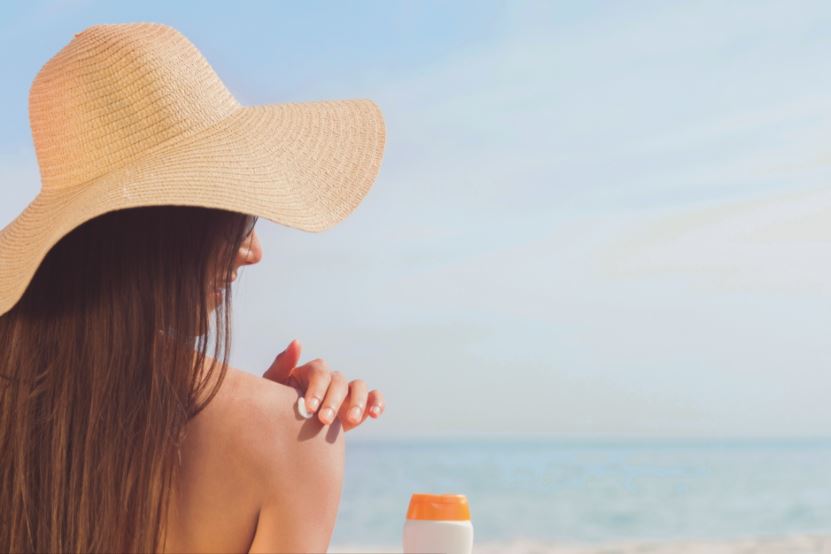 Mulher passando protetor solar na praia de chapéu