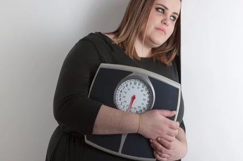 Mulher com sobrepeso abraçando uma balança