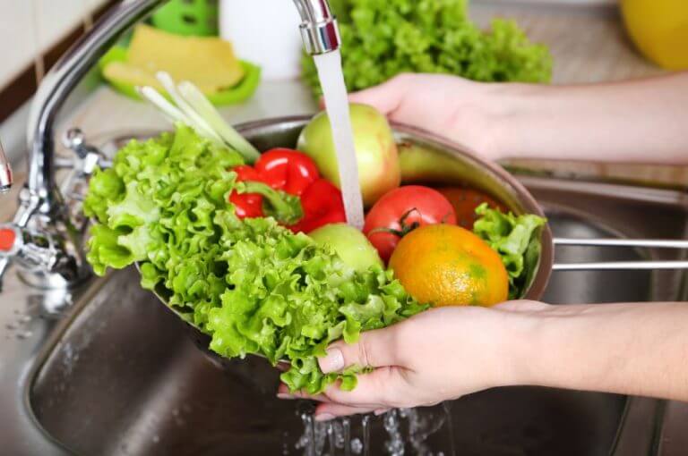 Mulher lavando vários legumos e verduras na pia