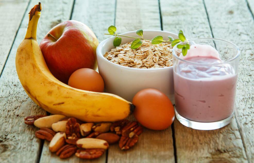Vários alimentos de café da manhã como banana, maça, oleaginosas, granola e iogurte
