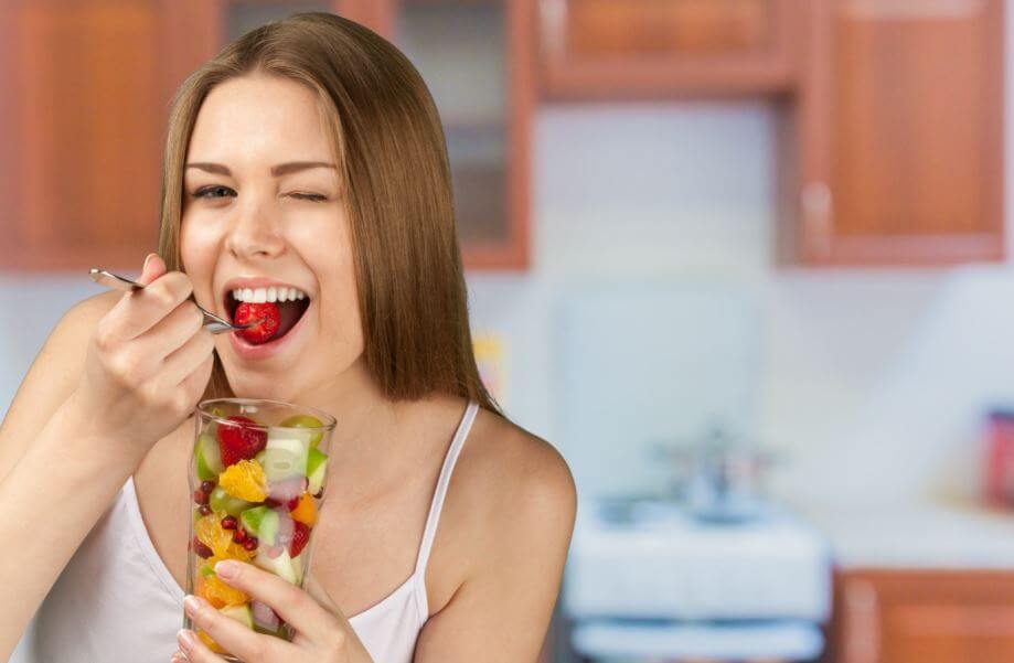 Mulher comendo um pote de frutas cortadas