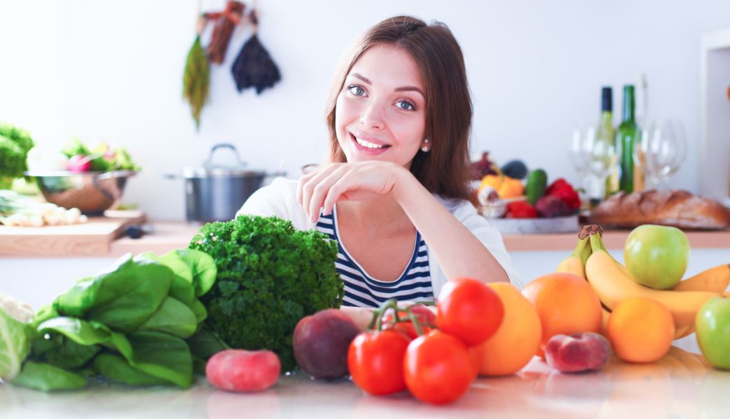 Mulher diante de várias frutas, legumes e verduras