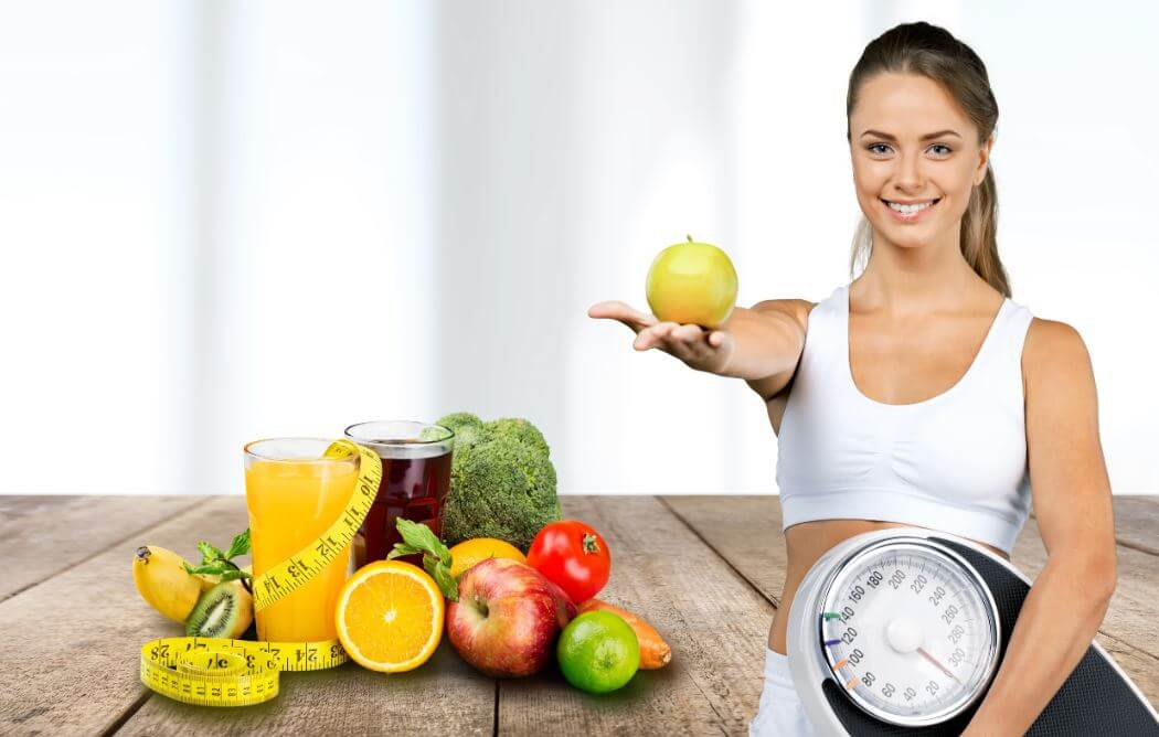 Garota oferecendo fruta diante de alimentos saudáveis com uma balança na mão