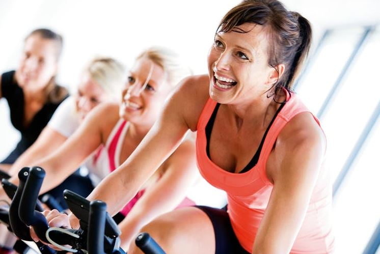 Spor salonunda kondisyon bisikletinde çalışan mutlu kadınlar.