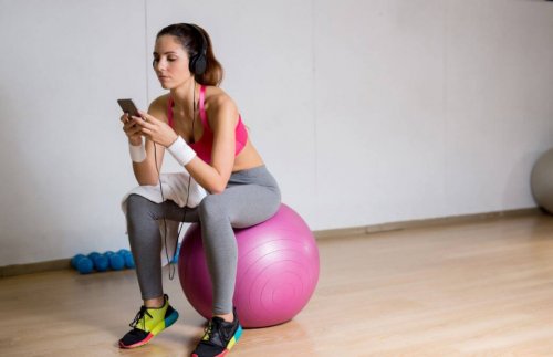 Pilates topunun üzerine oturmuş telefonuna bakan kadın.