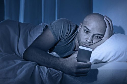 mand der ligger i sin seng og kigger på sin mobil 
