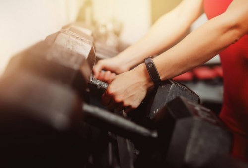 arms with fitness watch reaching for dumbbells