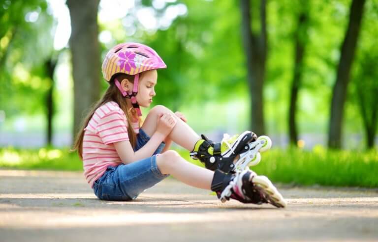 lille pige der sidder på asfalt med rulleskøjter og cykelhjelm på