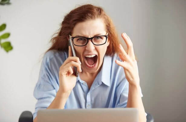 frustreret kvinde der snakker i mobil ved sin computer