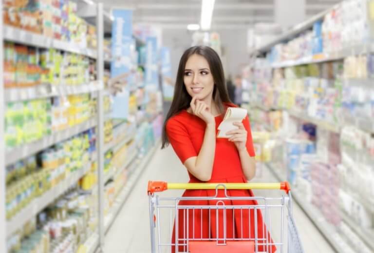 kvinde med indkøbsvogn og liste i supermarked