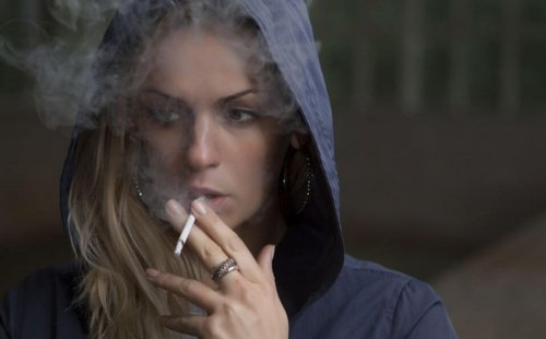 kvinde i hættetrøje der ryger en cigaret