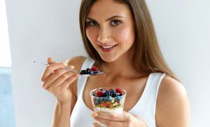 Woman eating yogurt with berries during breakfast. 