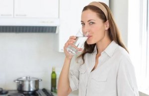 Woman drinking a glass of water in her kitchen.