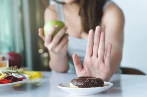 Woman rejecting unhealthy foods and eating a piece of fruit instead.