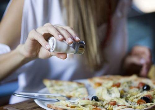 Woman sprinkling salt on her food plate due to a nutritional myth about low sodium products