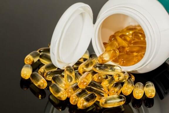 pilleglas med omega-3 piller der er hældt ud på et bord