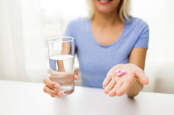 kvinde med et glas vand i den ene hånd og piller i den anden