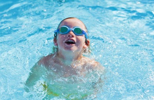 Child with goggles swimming in pool smiling