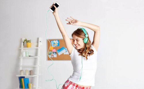 Young woman dancing at home with phone and headphones bailonga application